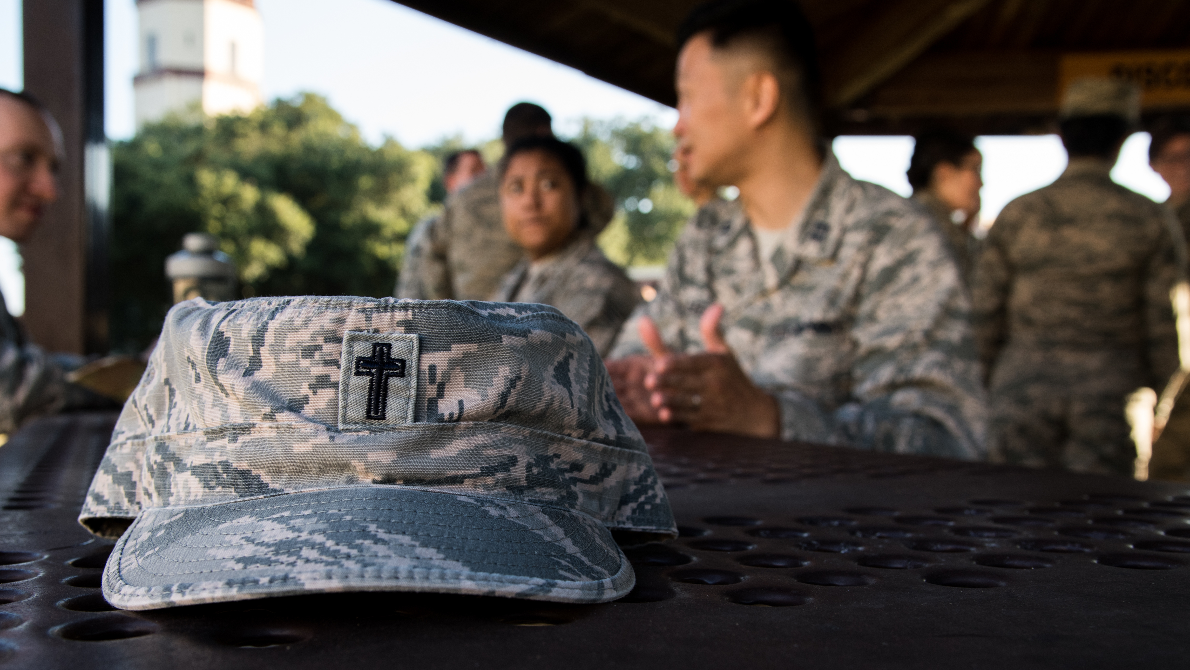 A U.S. Air Force chaplain's cover rests on a table as a service member discusses faith-related concerns during a religious service. (U.S. Air Force photo by Airman 1st Class Jacob B. Wrightsman) 