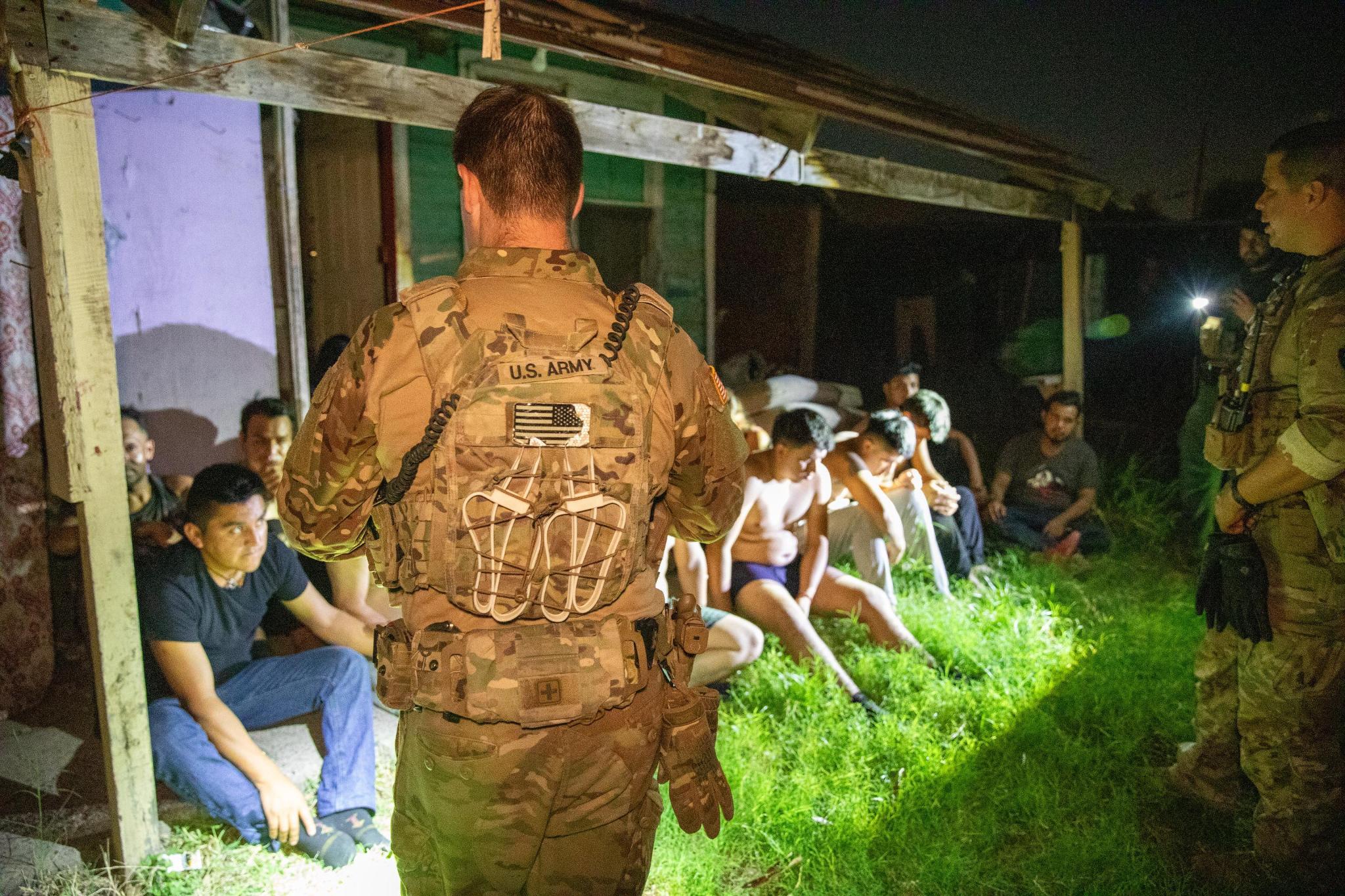 Soldiers stand outside a house at night