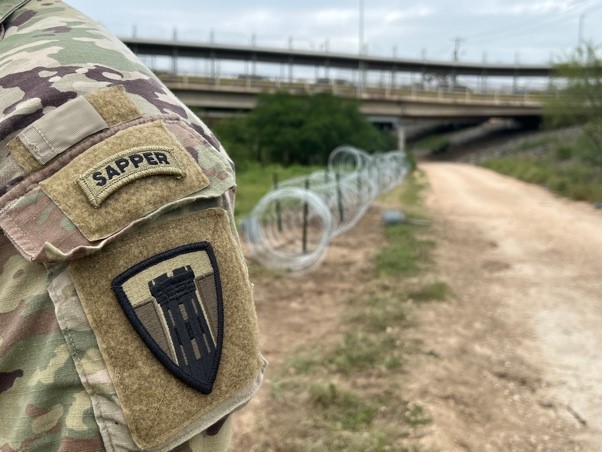 Soldier's shoulder patch standing in front of a concertina wire fence